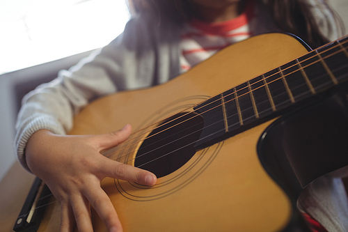 Mid section of girl practicing guitar at music class