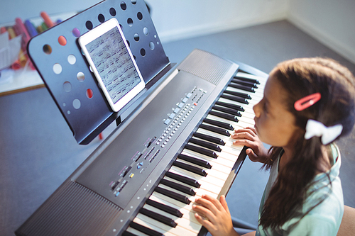 Elementary girl looking at digital tablet on stand while practicing piano in class at school