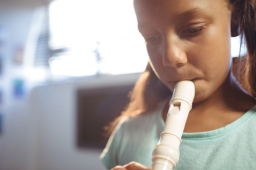 Thoughtful girl playing flute in classroom at music school