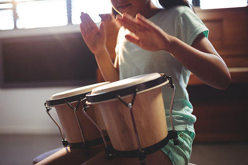 Mid section of girl playing bongo drums in classroom at music school