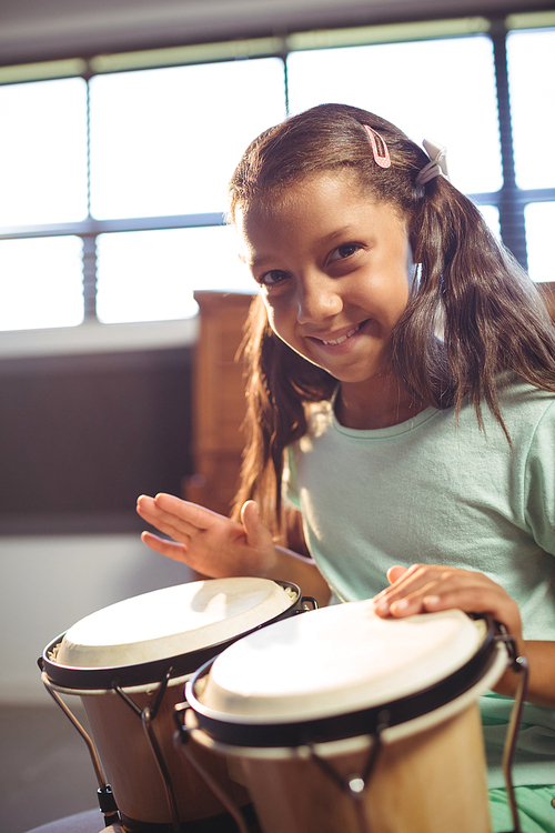 Portrait of smiling girl playing bongo drums in classroom at music school