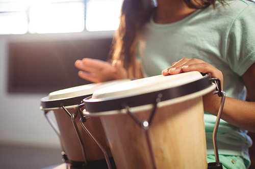 Mid section of girl playing bongo drums in classroom at music school