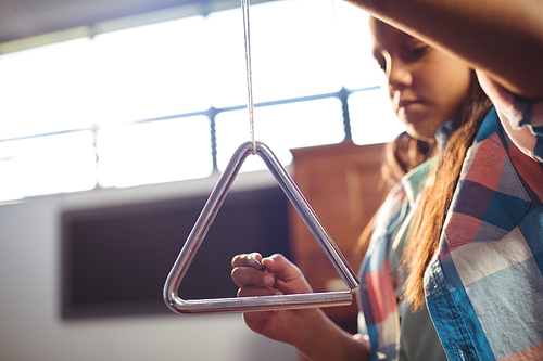 Low angle view of girl playing triangle in classroom at music school