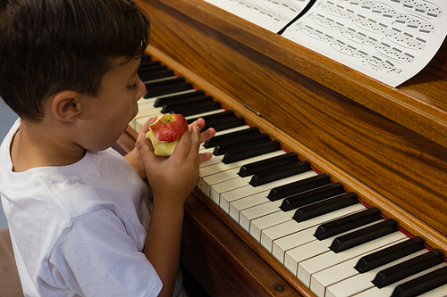 High angle view of boy eating apple while sitting by piano at home