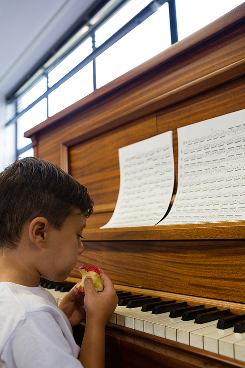 Close up of boy eating apple while sitting by piano at home