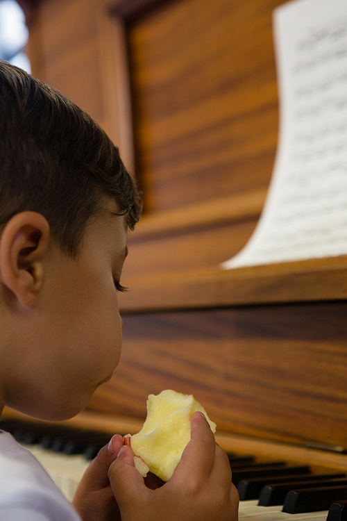 Close up of cute boy eating apple while sitting by piano at home