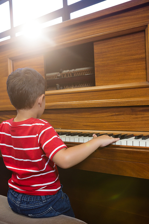 Rear view of boy playing piano in classroom at school