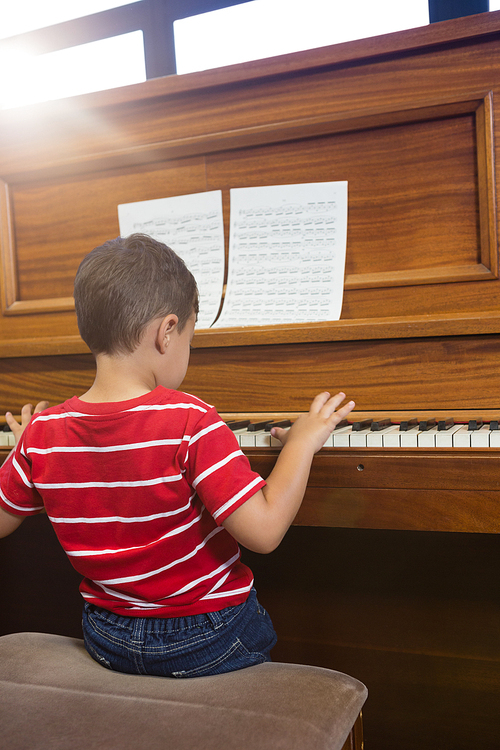 Rear view of cheerful friend playing piano while sitting in classroom at school