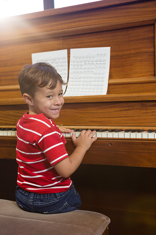 Portrait of smiling boy playing piano while sitting in classroom at school