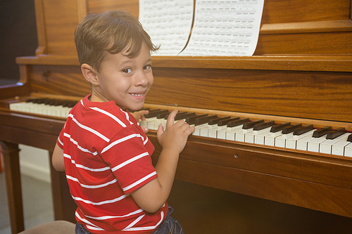 Portrait of cheerful boy playing piano while sitting in classroom at school