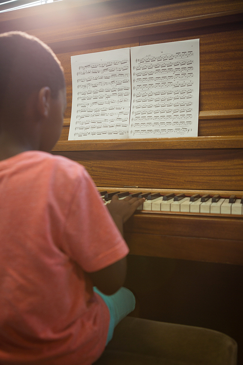 Rear view of boy practising piano in classroom at school