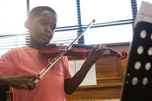 Boy playing violin while sitting in classroom at school