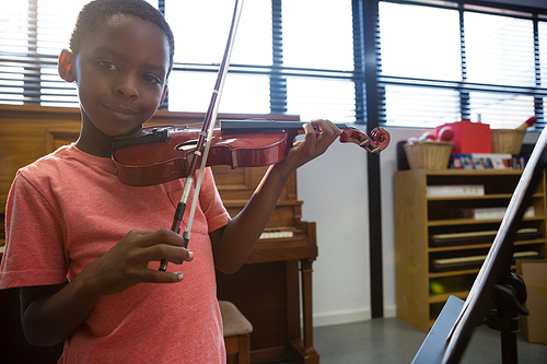 Portrait of smiling boy playing violin while standing in classroom at school