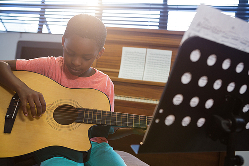 Boy playing guitar while sitting in classroom at school