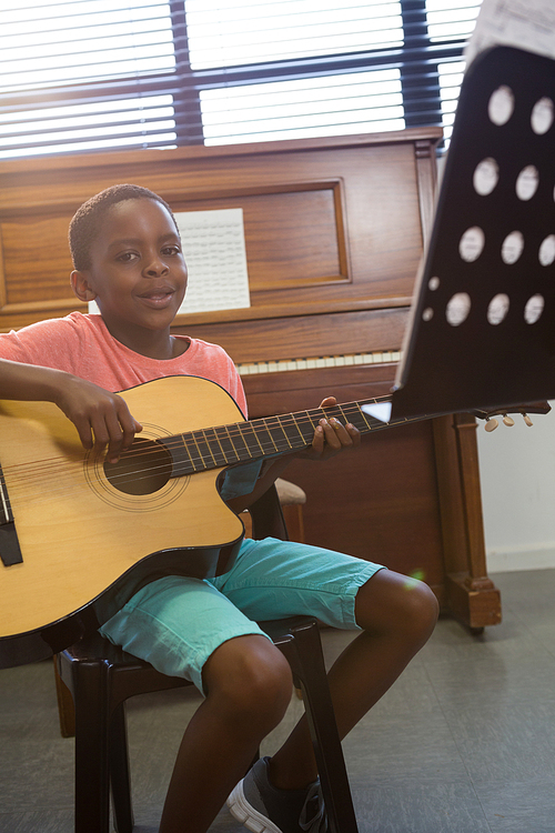 Portrait of boy playing guitar while sitting in classroom at school