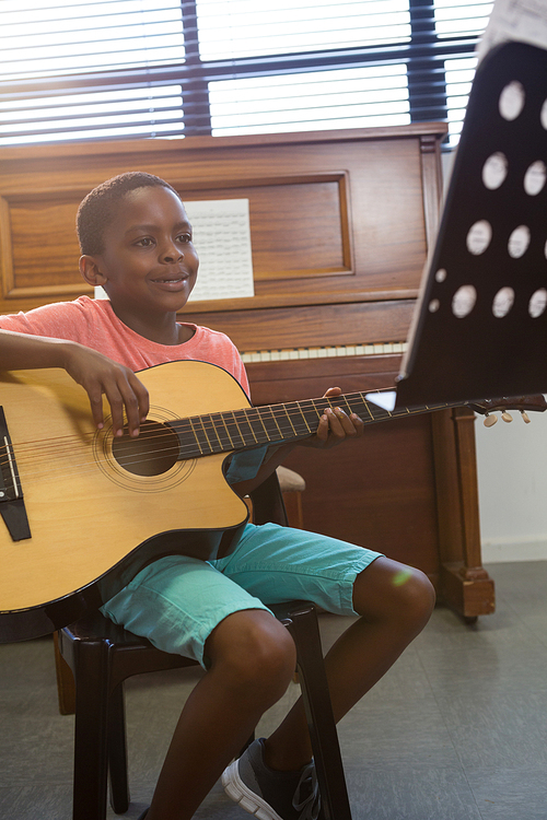 Happy boy playing guitar while sitting in classroom at school