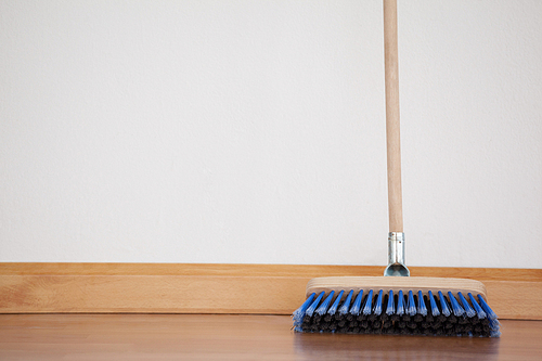Sweeping broom with wooden handle on floor against wall