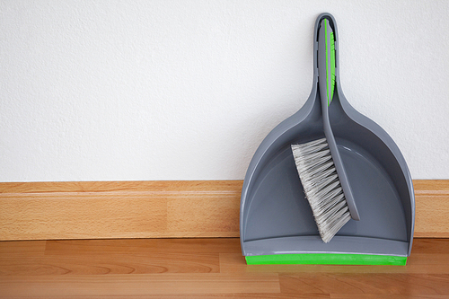 Close-up of dustpan and sweeping brush leaning against white wall