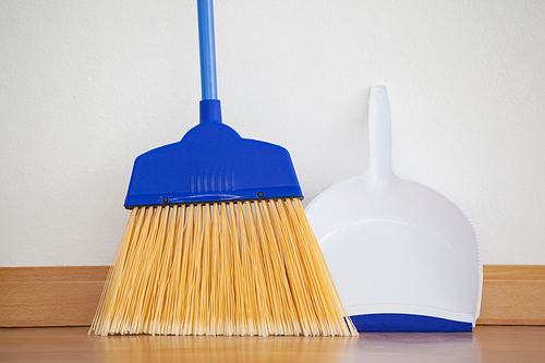 Close-up of dustpan and sweeping broom leaning against white wall