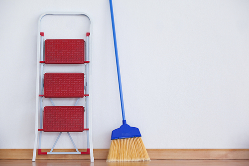 Ladder and sweeping broom leaning on white wall