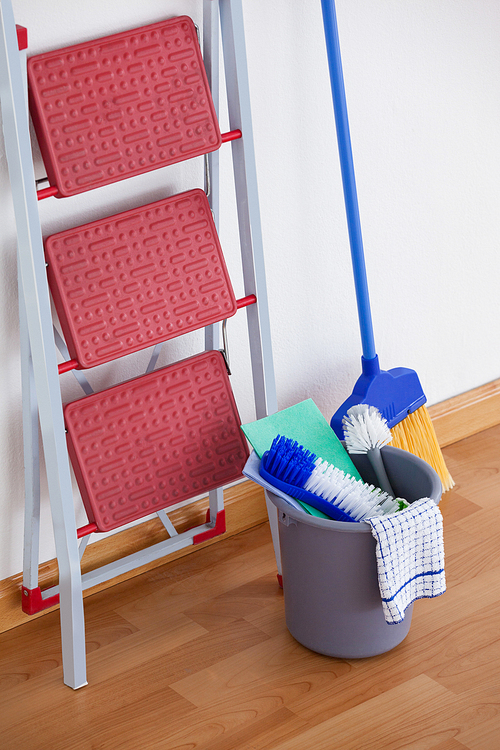 Ladder and cleaning equipment on wooden floor against wall