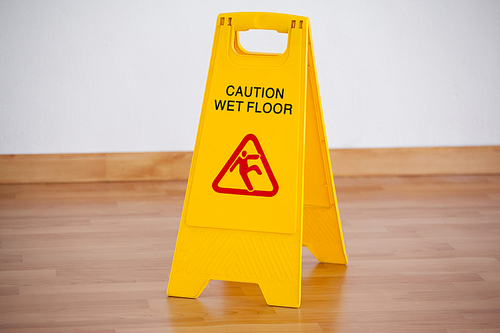 Close-up of wet floor caution sign on wooden floor