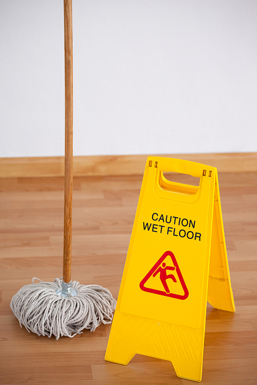 Mop with wet floor caution sign on wooden floor