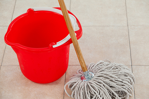 Close-up of empty bucket and mop on tile floor