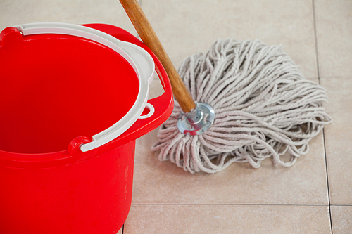 Close-up of empty bucket and mop on tile floor
