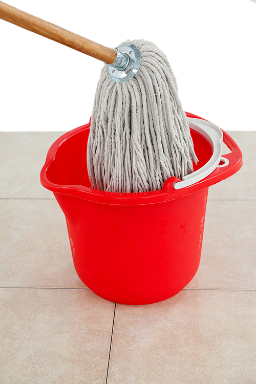 Mop in red bucket on tile floor against white wall