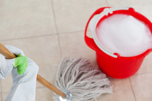 Red bucket with foamy water and mopping the tile floor