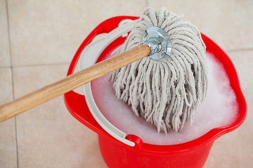 Red bucket with foamy water and mopping the tile floor