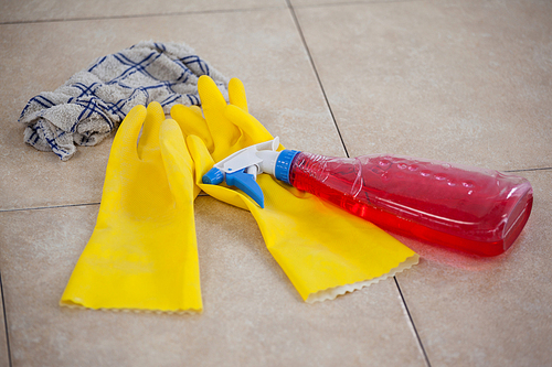 Close-up of detergent spray bottle, glove and cloth on tile floor