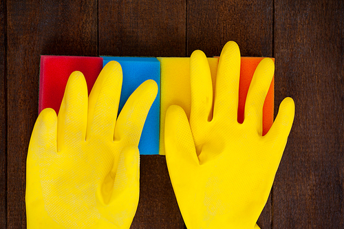 Close-up of yellow gloves with scouring pad on a wooden floor