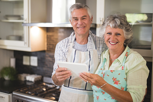 Portrait of smiling senior couple holding digital tablet in kitchen at home