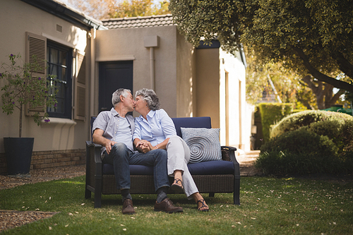 Senior couple kissing while sitting on couch in backyard