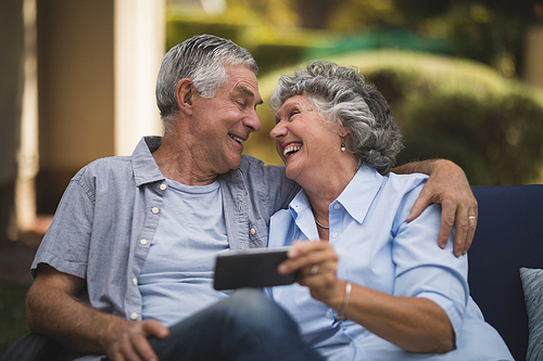 Cheerful senior couple looking at each other while sitting on sofa in backyard