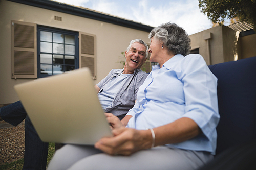 Happy senior couple sitting together with laptop on couch in backyard