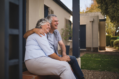 Happy senior couple embracing while sitting by house in backyard