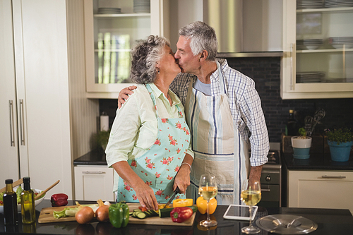 Senior couple kissing while preparing food in kitchen at home