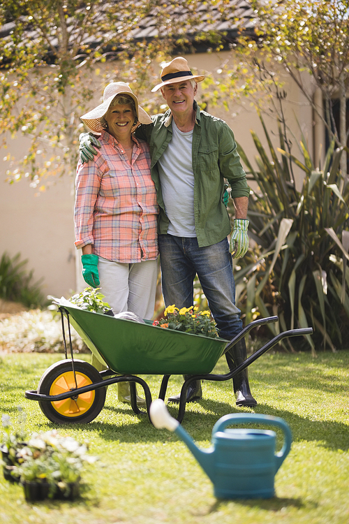 Portrait of smiling senior couple standing by wheel borrow on field in yard