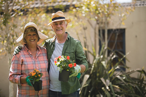 Portrait of smiling senior couple holding potted plants while standing in yard