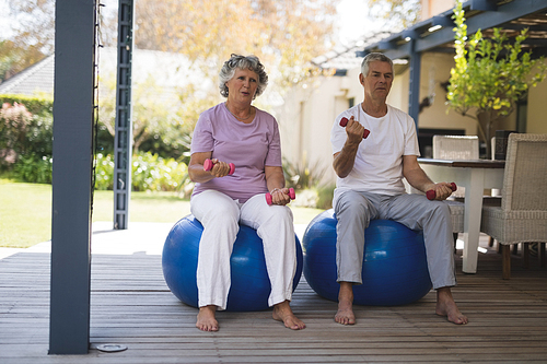 Full length of senior couple exercising while sitting on balls at porch