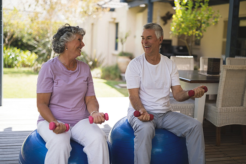Happy senior couple exercising together while sitting on balls at porch