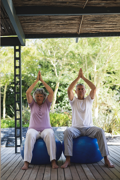 Full length of senior couple meditating sitting together on blue exercise balls at porch