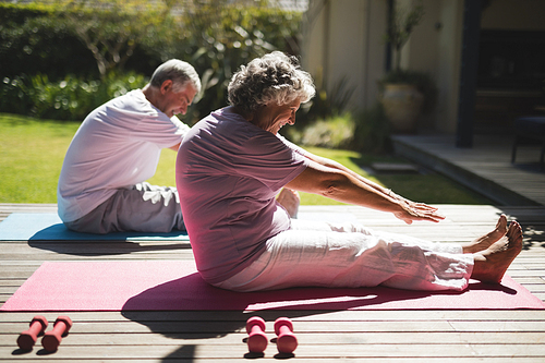 Senior couple exercising together while sitting on mat at porch