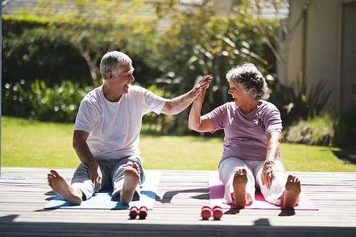 Cheerful senior couple giving high five while exercising together on mat at porch