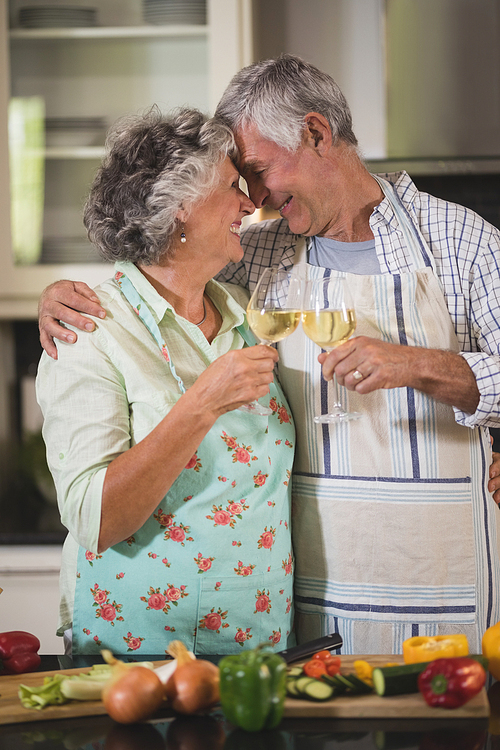 Happy senior couple toasting wine glasses while standing together in kitchen at home