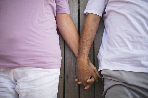 Overhead mid section of senior couple holding hands while lying on porch