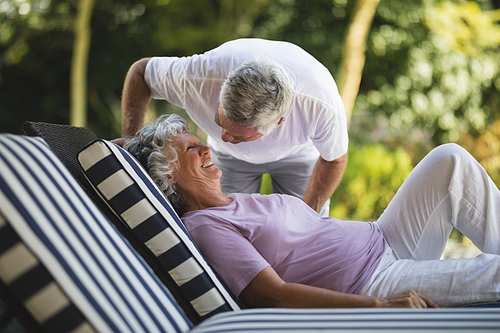 Senior man bending over smiling woman resting on lounge chair